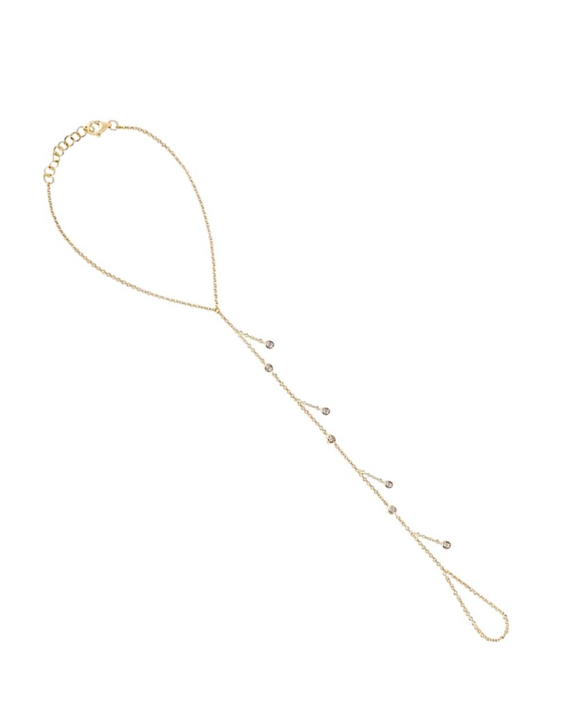Gold hand chain with seven bezel-set diamond charms cascading along a delicate chain, connecting the wrist to a finger loop.
