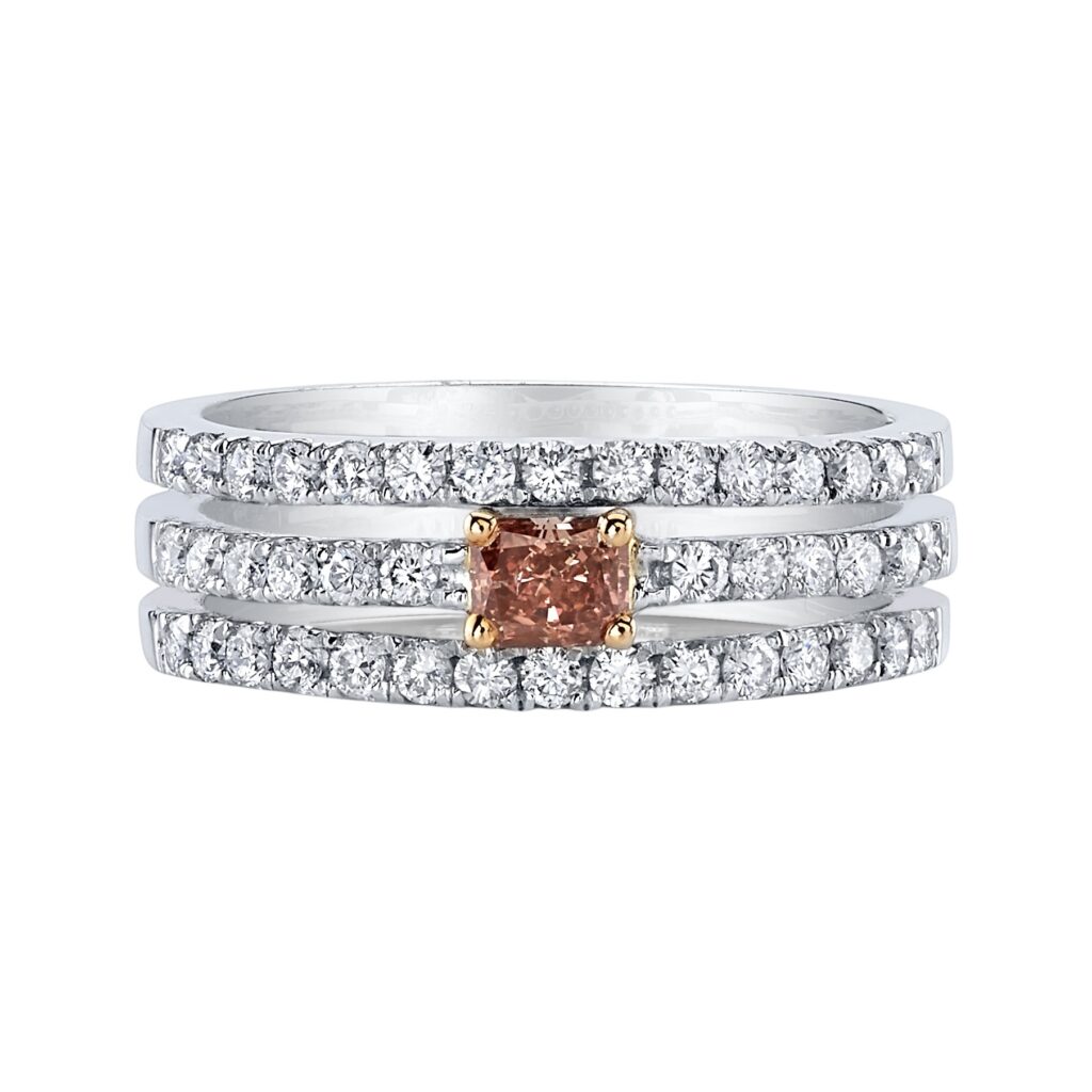 Platinum ring with three rows of round white diamonds and a deep pink cushion-cut center diamond set in yellow gold prongs.