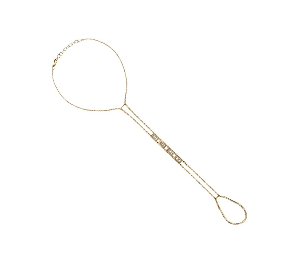 Gold hand chain styled on a model’s hand, featuring a fine chain with rectangular baguette diamonds connecting a bracelet to a ring, shown on a neutral background.